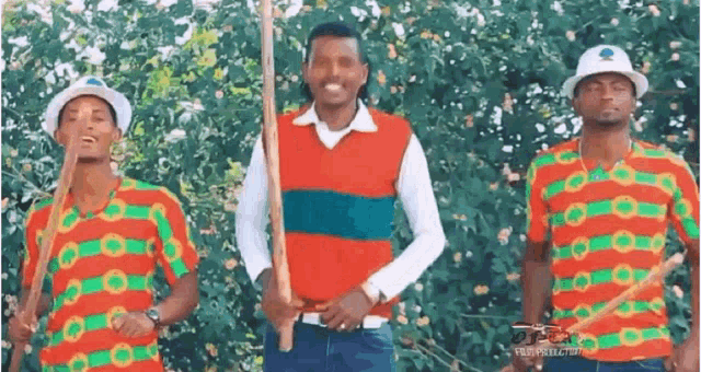a group of men are standing next to each other holding sticks and wearing colorful shirts .