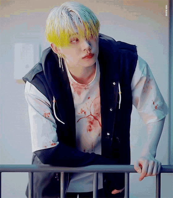 a young man with yellow hair leaning on a railing