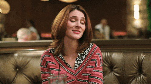 a woman in a pink sweater sits on a brown couch