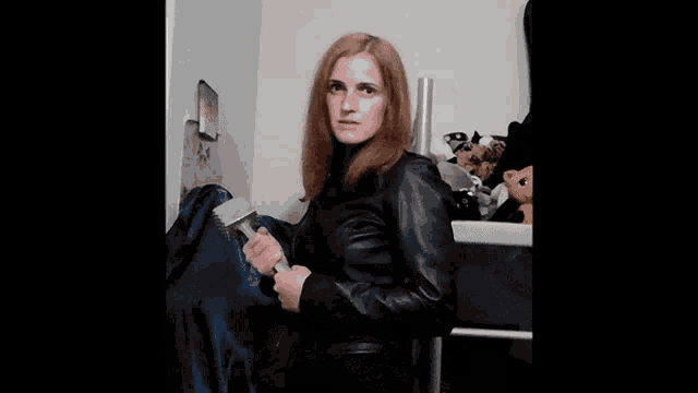a woman with long red hair is wearing a black leather jacket and smiling for the camera .