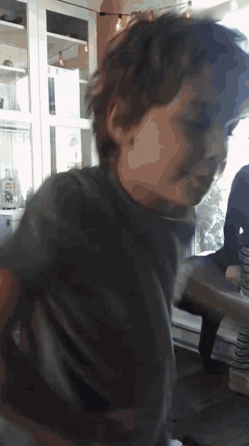 a young boy in a gray shirt is smiling in a kitchen