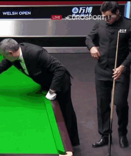 two men playing pool in front of a welsh open banner