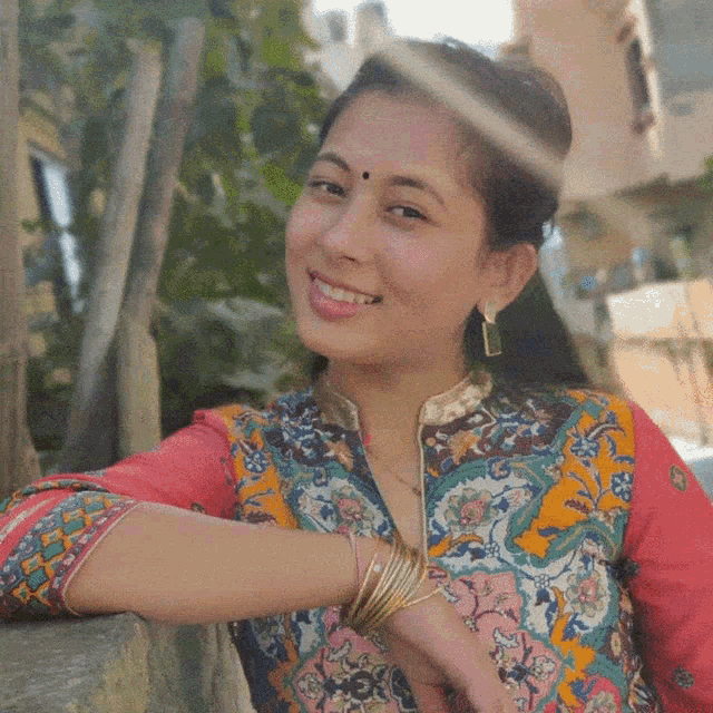 a woman with a bindi on her forehead is smiling and wearing a colorful shirt