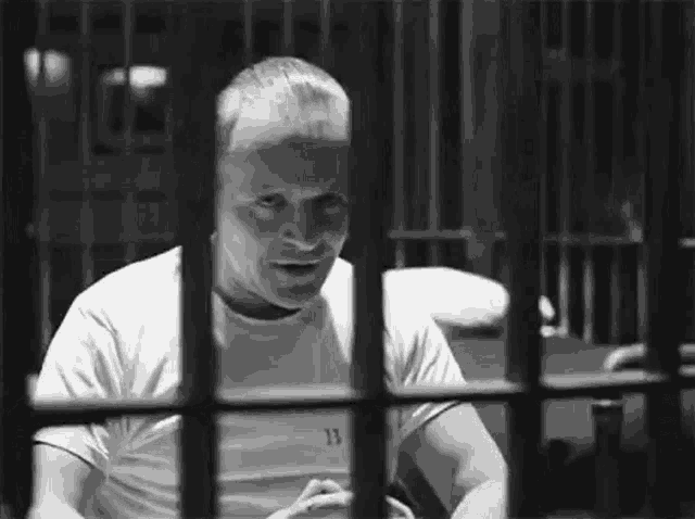 a man is sitting in a jail cell behind bars and looking through the bars .