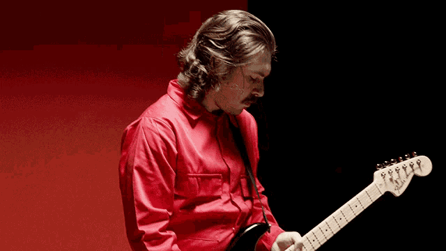 a man in a red shirt is playing a fender electric guitar