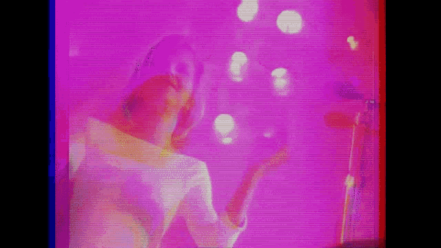 a woman is singing into a microphone while standing in front of a pink wall .
