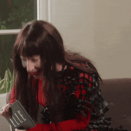 a woman is sitting on a couch reading a book called elle