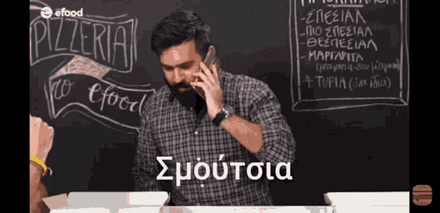 a man is talking on a cell phone in front of a blackboard that says pizzeria
