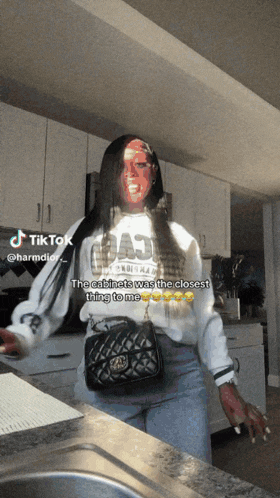 a woman is standing in a kitchen wearing a white shirt that says " the cabinets was the closest thing to me " on the front