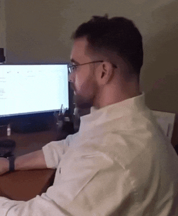 a man wearing glasses sits in front of a computer monitor
