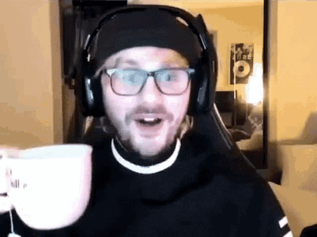 a man wearing glasses and headphones is holding a cup of coffee .