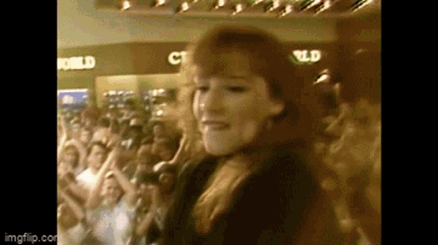 a woman with red hair is dancing in front of a crowd with a sign that says world in the background
