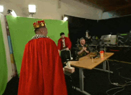 a man wearing a red cape and a crown stands in front of a green screen