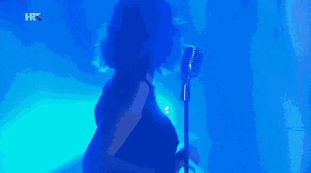 a woman singing into a microphone with a blue background and the letters hrc on the bottom