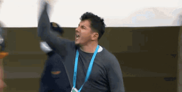 a man wearing a lanyard around his neck is raising his arms in the air .