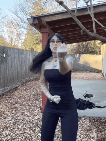 a woman in a black dress giving the middle finger in front of a wooden fence