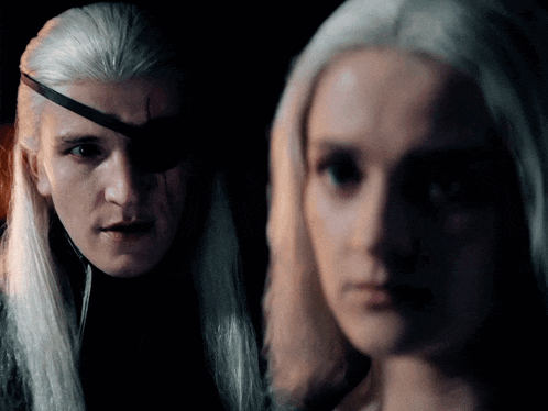 a man with a bandage on his eye is standing next to a woman with long white hair