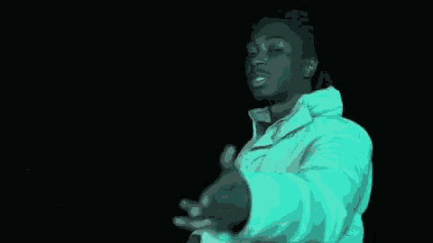 a man in a white jacket is holding a bottle of soda and making a peace sign with his hands .