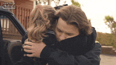 a man and a girl hugging in front of a car that says son of a glitch on it