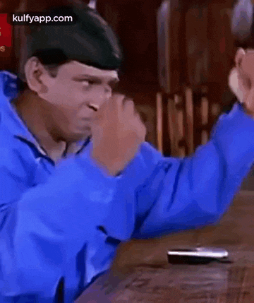 a man in a blue jacket is sitting at a table with his hands in the air .