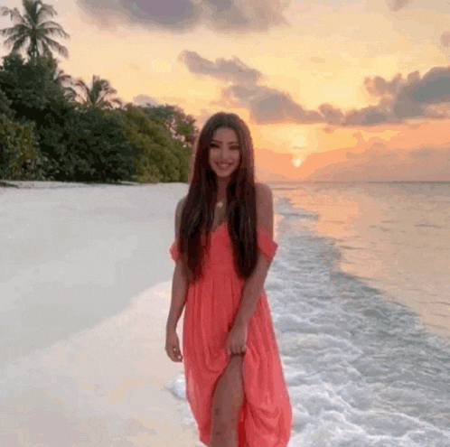 a woman in a red dress is standing on a beach .