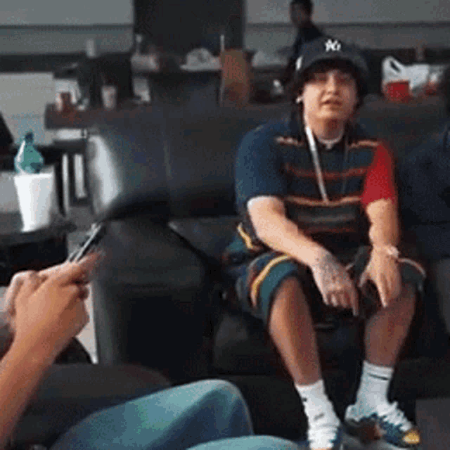 a man is sitting on a couch wearing a hat and a striped shirt .