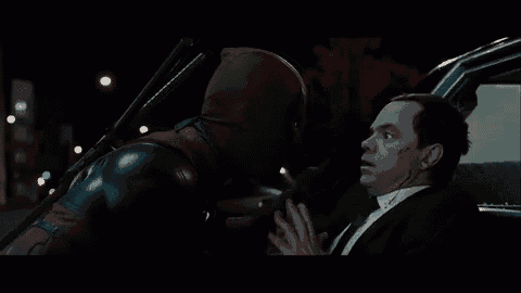 a man in a suit and tie is talking to deadpool in a car .