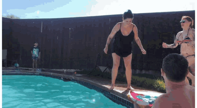 a woman jumps into a swimming pool while a boy watches