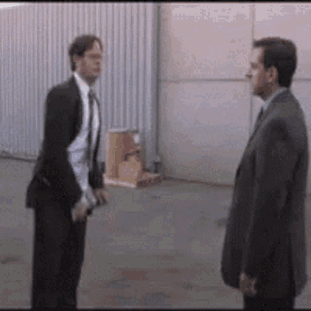 two men in suits are standing next to each other in a parking lot .