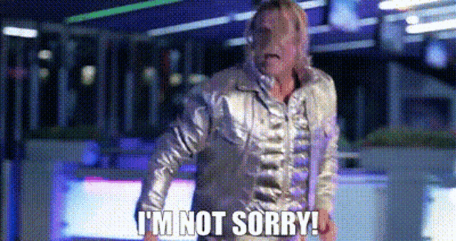 a man in a silver jacket is standing in a room and saying `` i 'm not sorry ! ''