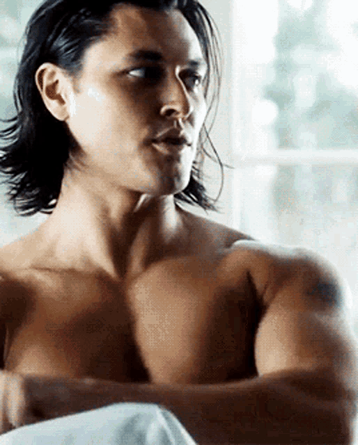 a shirtless man with long hair is laying in bed