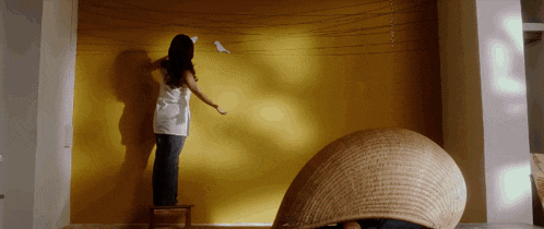 a woman is standing on a small stool painting a yellow wall