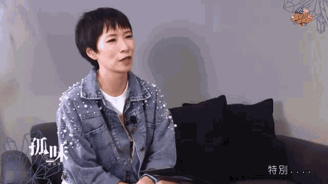 a woman in a denim jacket with pearls on the sleeves sits on a black couch