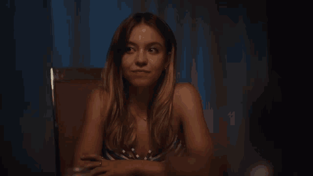 a woman is sitting at a table in a dark room looking at the camera .