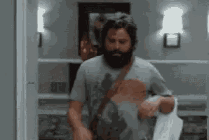 a man with a beard is standing in a hallway holding a piece of paper .