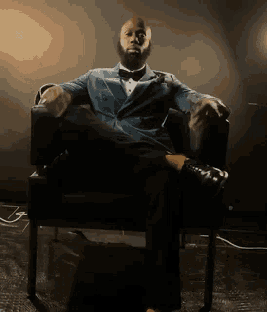 a man in a suit and bow tie is sitting in a chair with his legs crossed
