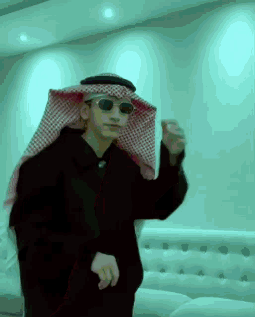a man wearing sunglasses and a keffiyeh is dancing in a room