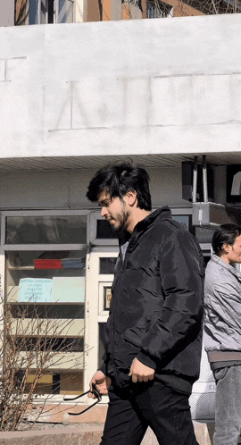 a man in a black jacket is walking in front of a building that says t.