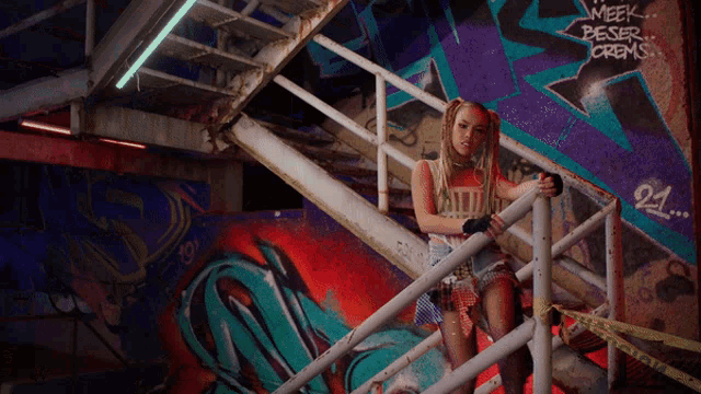 a woman stands on a set of stairs in front of a wall with graffiti that says meek