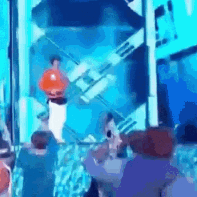 a man in an orange shirt is standing in front of a crowd of people