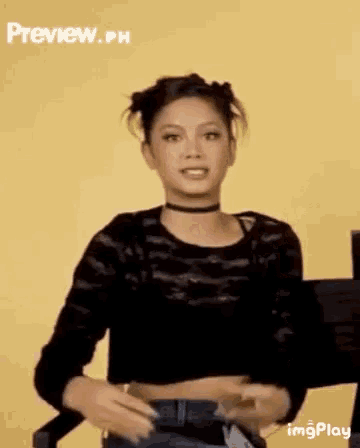 a woman wearing a choker and a black crop top is standing in front of a yellow background .