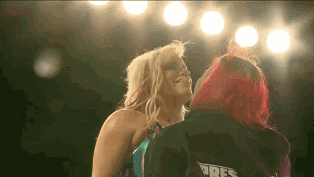 two women are kissing each other in a wrestling ring in front of a crowd .