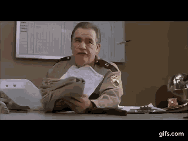 an older man in a sheriff 's uniform is sitting at a desk holding a bag of money .