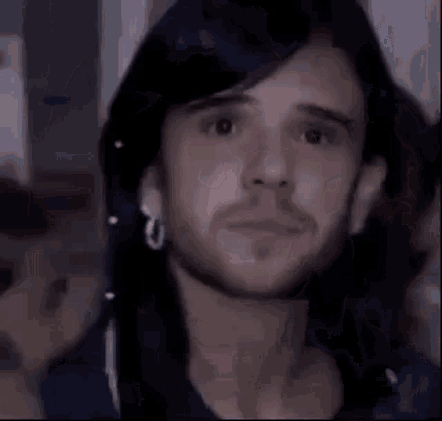 a man with long black hair and a beard is wearing earrings and looking at the camera .