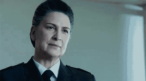 a woman in a uniform and tie is looking at the camera with a serious look on her face .