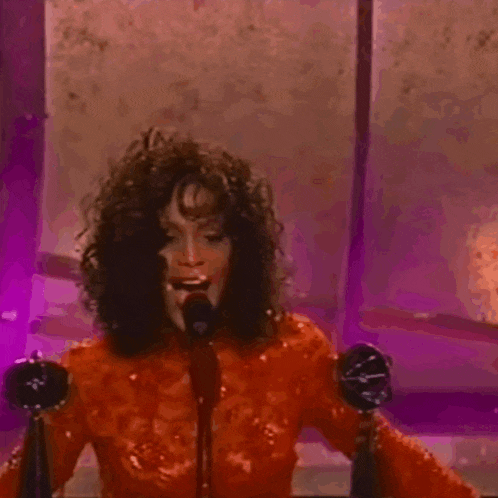 a woman in a red dress is singing into a microphone in front of a purple wall .