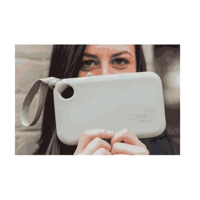 a woman covering her face with a gray via via purse