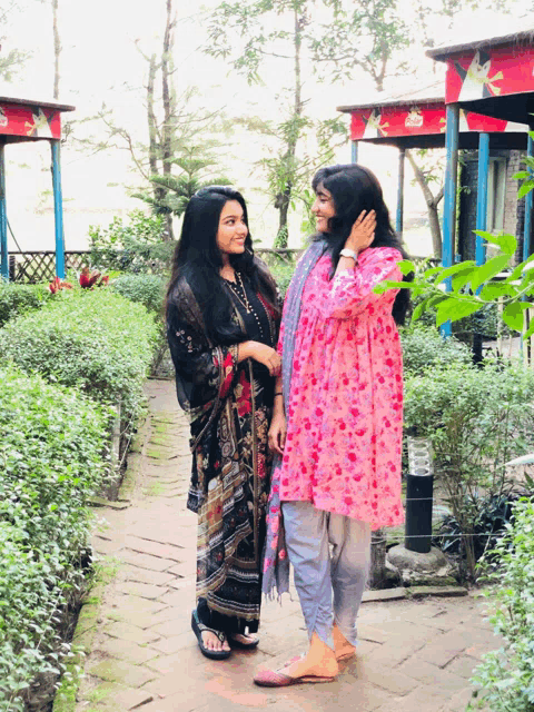two women standing next to each other in front of a building with flowers on it