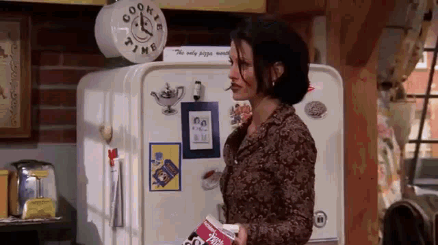 a woman is standing in front of a refrigerator in a kitchen holding a bag of chips .