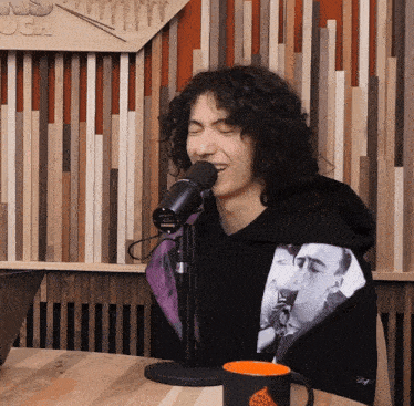 a man with curly hair singing into a microphone in front of a wooden wall that says ugh